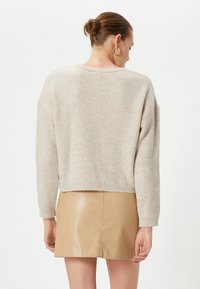Beżowy sweter z prążkowanego dzianiny o skróconym kroju i opuszczonych ramionach, zestawiony z błyszcząca beżową spódnicą mini z sztucznej skóry.