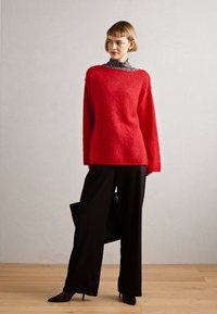 Rød, lodden genser med lange ermer lagdelt over en svart-hvitt stripete turtleneck, pairt med svarte vide bukser og hæler.
