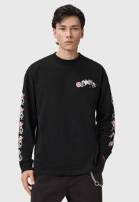 Camiseta negra de manga larga hecha de algodón. Presenta impresiones gráficas coloridas en el pecho y las mangas, con un ajuste holgado y cuello redondo.