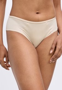 Beige Bikiniunterhosen mit glatter Textur und gerippten Seiteneinsätzen, ausgestattet mit einem mittelhohen Schnitt und subtilem Stich entlang der Kanten.