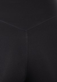 Leggings neri a vita alta realizzati in tessuto elastico, con cuciture piatte e una superficie liscia. Nessun motivo o hardware visibili.