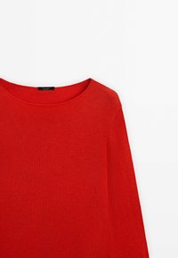 Pull-over en tricot rouge vif à manches longues avec un col rond, présenté sur un fond blanc uni.