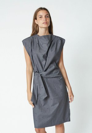 Rochie gri fără mâneci, cu un design drapat și un nod pe lateral. Prezintă un model texturat subtil și o siluetă dreaptă. Material moale.