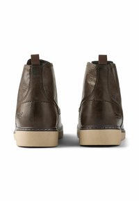 Botas de tobillo de cuero marrón con una textura suave, suelas beige y costuras marrones. Cuentan con un tirador en la parte trasera para facilitar el uso.