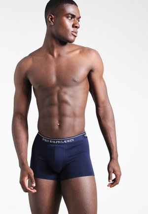 Marineblaue Boxershorts mit einem engen Schnitt, ausgestattet mit einem Logo-Bund. Glattes Material mit einem klassischen Design. Das Model zeigt die Shorts im Stehen.