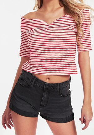 Top corto de rayas rojas y blancas con escote off-the-shoulder y mangas cortas, combinado con pantalones cortos de mezclilla negros de talle alto con dobladillos enrollados.