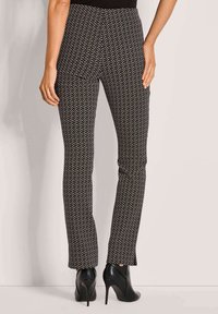 Zwarte broek met een wit zigzagpatroon, slim fit en een gladde textuur, gecombineerd met zwarte hoge enkellaarsjes.