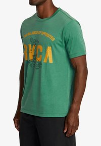 Green cotton t-shirt with short sleeves, round neck, and printed graphic featuring text and an illustration in yellow and black.