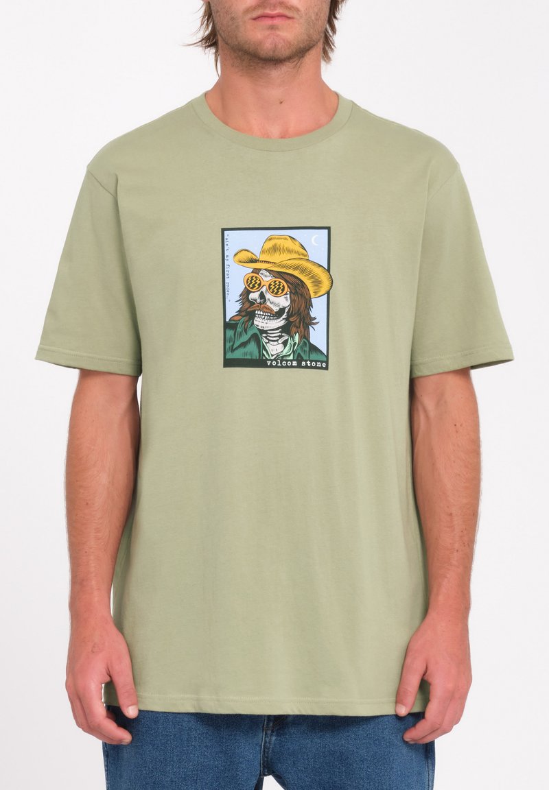 Camiseta de algodón color verde olivo con un vibrante gráfico de un esqueleto que lleva gafas de sol y un sombrero amarillo, con mangas cortas y un corte relajado.