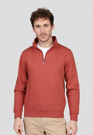 Sweat-shirt zippé rouge en mélange de coton doux, avec un col relevé, des poignets côtelés et un détail de logo sur la poitrine.