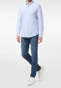 Jasnoniebieska koszula z długim rękawem i kołnierzykiem zapinanym na guziki, w połączeniu z ciemnoniebieskimi dżinsami i białymi trampkami. Teksturowany materiał, standardowy krój.