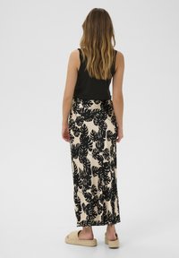 Beige színű virágmintás szoknya fekete levélmintázattal, maxi hosszúsággal és laza szabással. Fekete ujjatlan toppal és szandállal párosítva.