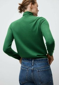 Pulover verde cu guler înalt realizat din țesătură tricotată, asortat cu blugi albaștri cu talie înaltă. Are un design mulat și guler cu dungi.