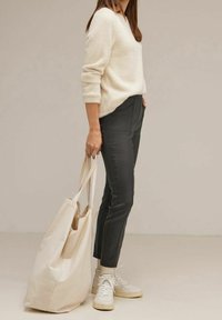 Ljus krämfärgad stickad tröja, mörkgrå skräddarsydda byxor, vita sneakers och en stor krämfärgad toteväska med långa handtag. Släta texturer genom hela outfiten.