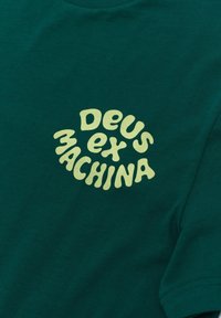 Green cotton t-shirt featuring a rounded, light yellow graphic that reads "Deus ex Machina" in a wavy, playful font.