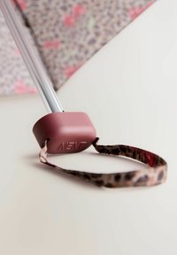 Rosa gummihåndtag med "NEXT" præget, fastgjort til en metalk pole. Har et leopardmønster bånd, der strækker sig fra håndtaget.