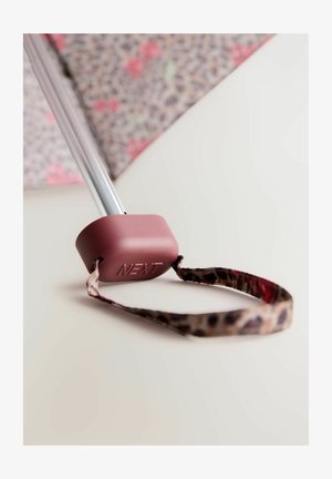 Roze rubberen handgreep met "NEXT" erop gedrukt, bevestigd aan een metalen paal. Bevat een leopardenprintband die van de handgreep uitsteekt.