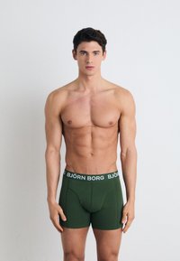 Green boxer briefs with a snug fit, featuring a white elastic waistband labeled "BJÖRN BORG." Smooth texture and no visible patterns.