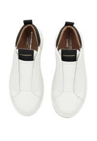 Sneaker bianche senza lacci con linguette nere sul tallone e etichette nere sulla lingua che riportano "Alexander Smith," viste dall'alto.