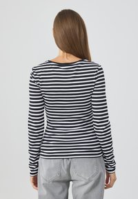 Long-sleeve striped top in black and white, featuring a round neck and a fitted design. The fabric appears soft, with a smooth texture.