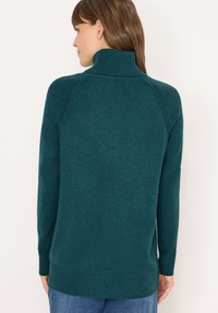 Maglione a collo alto in maglia color teal con maniche lunghe, polsini e orlo a coste, caratterizzato da una finitura testurizzata e un design dal taglio rilassato.