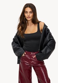 Zwarte leren oversized jack gedragen over een zwarte bodysuit, gecombineerd met hooggetailleerde bordeauxrode broek met krokodillenpatroon. Gouden creolen.