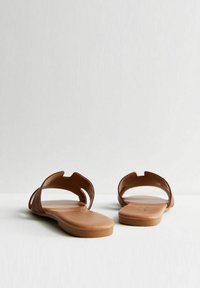 Sandali piatti marroni con punta aperta, caratterizzati da due fasce larghe. Texture in pelle liscia e suola marrone chiaro. Design minimalista.