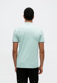 Világos menta zöld rövid ujjú galléros póló, puha anyaggal, kontrasztos szegéllyel a galléron és a mandzsettán, klasszikus szabású, hátulnézetben.