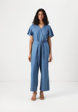Denim overal s V-výstřihem, volnými rukávy, opaskem v pase, širokými nohavicemi a ohrnutými lemy, v světlém modrém odstínu.