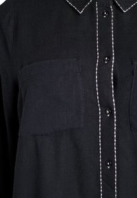 Čierna košeľa na gombíky s dvoma prednými vreckami, kontrastným bielym prešívaním pozdĺž goliera a gombíkovej légy. Hladká textúra, klasický dizajn.