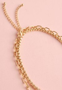 Zelta ķēdes kaklarota ar vairākiem savienotiem ķēdēm, kas atšķiras biezumā. Iekļauts sprādze un regulējama pagarinājuma ķēde.