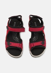 Raudoni sandalai su reguliuojamais dirželiais, juoda vidine pamušalu, guminis padas ir tekstūruoti akcentai. Su saugiu sagtimi.