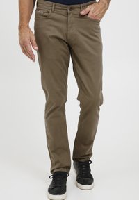 Slim-fit, olijfgroene katoenen chinos met voorkruiszakken en een knoopsluiting, gecombineerd met zwarte sneakers met witte zolen.