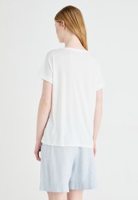 T-shirt blanc à manches courtes avec des poignets roulés, coupe décontractée et texture lisse, associé à un short bleu clair. Vue de dos.