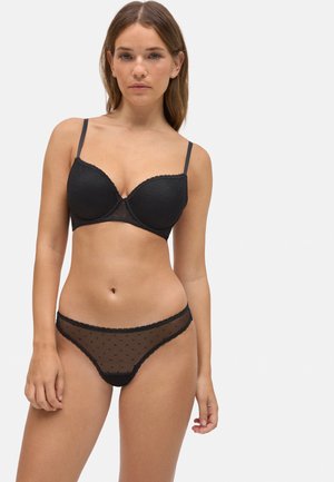 Sujetador negro acolchado con tirantes finos y tela texturizada; braguitas negras transparentes de lunares con bordes festoneados a juego.