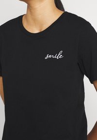 Černé bavlněné tričko s kulatým výstřihem a krátkým rukávem, s bílým vyšitým nápisem "smile" na levé části hrudi.