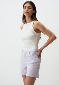 Shorts en coton violet clair avec une coupe droite, poches avant et une fermeture à bouton unique, associés à un débardeur ajusté blanc à côtes.