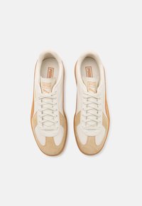 White and beige sneakers with leather and suede materials, featuring a lace-up design, round toe, and textured rubber sole.