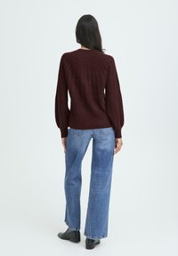 Maglione a maglia bordeaux con texture a coste e maniche a sbuffo, abbinato a jeans a gamba larga blu chiaro e stivaletti neri.