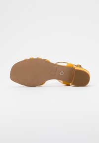 Sandal in suede giallo con suola quadrata, tacco basso a blocco, cinturino alla caviglia e suola in gomma texturizzata, mostrato dal basso.