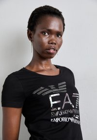Zwarte T-shirt met korte mouwen en reflectieve grafische print met "EA7 EMPORIO ARMANI." Zachte stof, getailleerde pasvorm, ronde hals.
