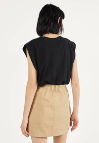 Svart kortärmad topp med vadderade axlar, kombinerad med en högmidjad beige denimkjol med elastisk midja och bakstygn.