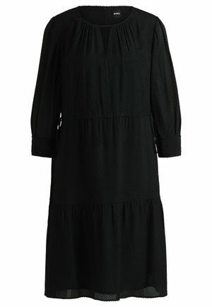 Robe midi noire texturée avec des manches longues, poignets à volants, taille froncée, et un léger décolleté en V avec des plis subtils.