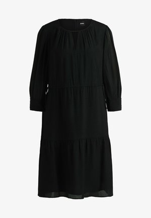 Robe midi noire texturée avec des manches longues, poignets à volants, taille froncée, et un léger décolleté en V avec des plis subtils.