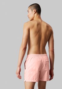 Costumi da bagno rosa chiaro con vita elasticizzata, tasche laterali e una tasca posteriore singola. Texture liscia e lunghezza sopra il ginocchio.