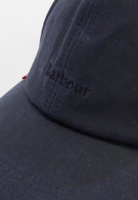 Boné de algodão azul-marinho com detalhes costurados, apresentando um logótipo da marca bordado na mesma cor na frente. Design de aba reta.