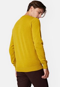 Żółty sweter z okrągłym dekoltem, długimi rękawami oraz ściągaczami na mankietach i u dołu. Materiał wydaje się miękki i teksturowany, noszony na ciemnych spodniach.