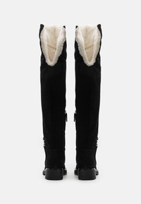 Botas de ante negras hasta la rodilla con un suave forro crema, cierre de cremallera y tacón plano. El diseño cuenta con un puño vuelto para mayor textura.