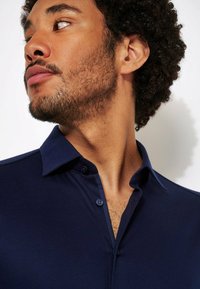 Navyblauw polo-shirt met een knoopsluiting op de kraag, korte mouwen en een gladde textuur, met een subtiele glans en contrasterende kraag details.