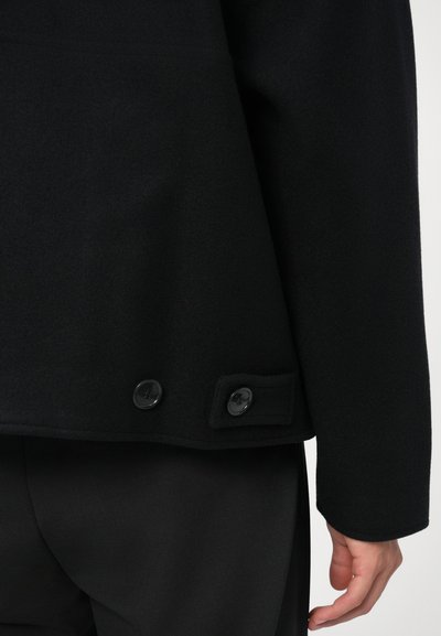 Must mustrikkidega must villasegu mantel, millel on tekstureeritud viimistlus, sirge lõikega, kaks musta nööpi vasakul küljel ja elegantne siluett.